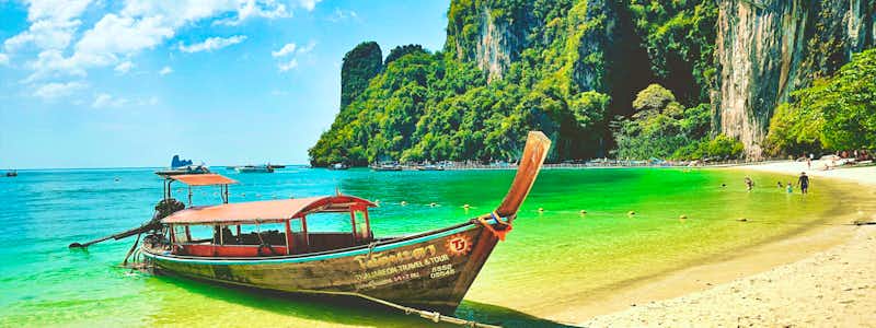 Tropischer Strand in Thailand mit Longtail-Boot und Kalksteinfelsen