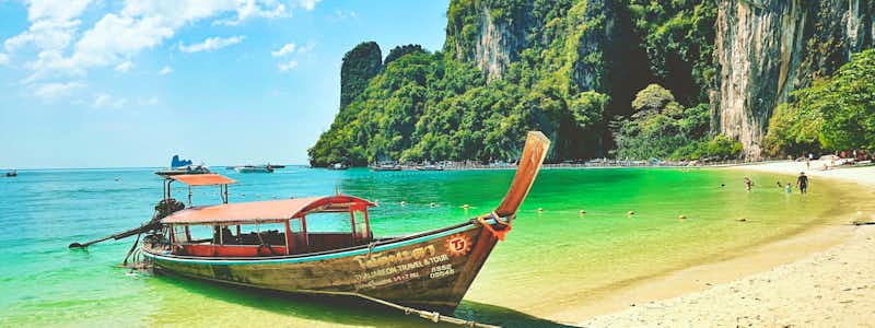 Tropischer Strand in Thailand mit Longtail-Boot und Kalksteinfelsen